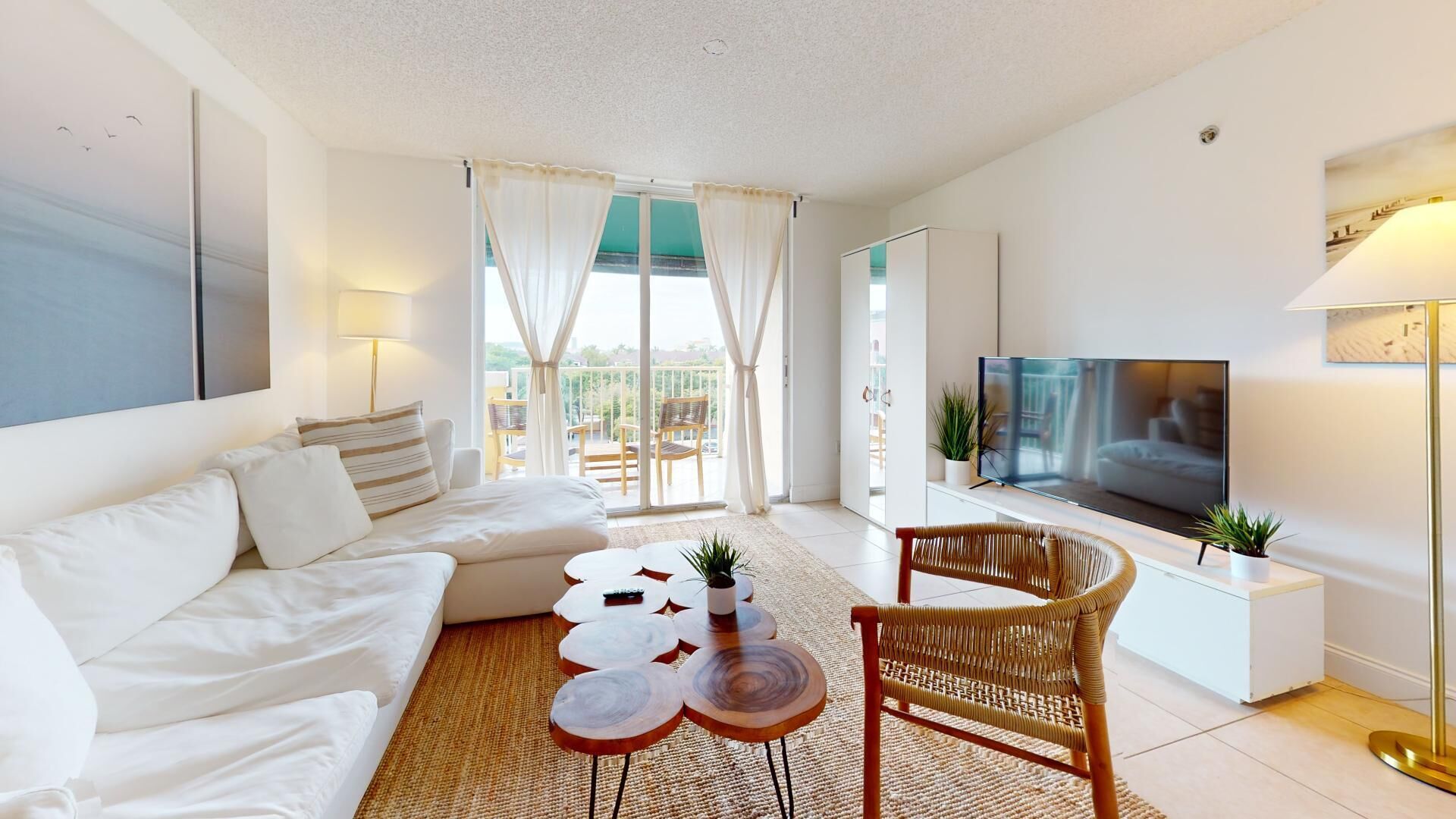 Una sala moderna con un sofá blanco, un televisor, una silla de mimbre y un balcón con vistas.