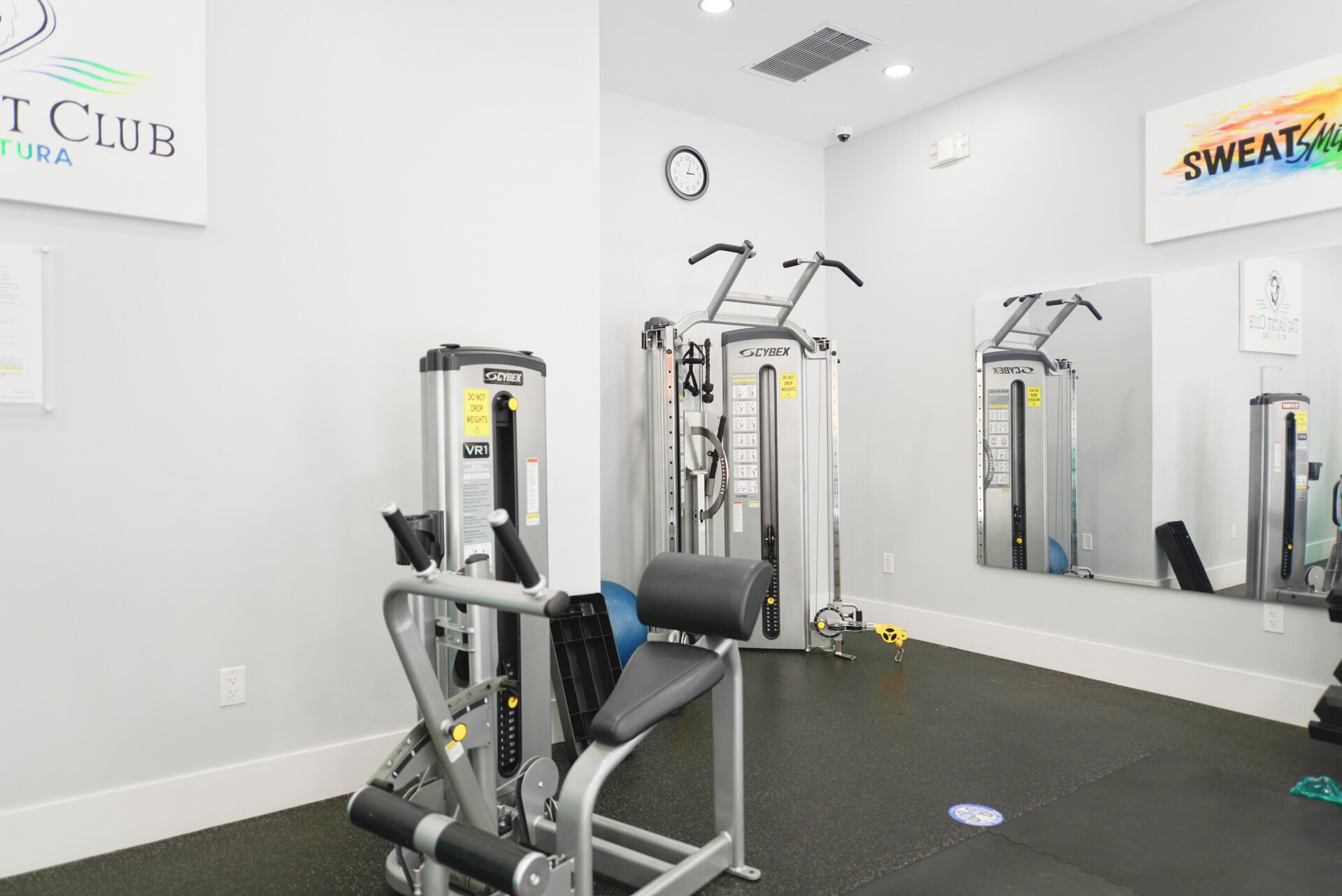 A gym with various exercise machines, a clock, and motivational posters on the walls.