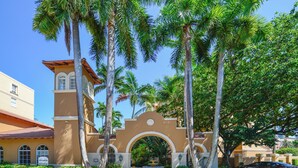 A building with a central archway, palm trees, and a paved entrance.