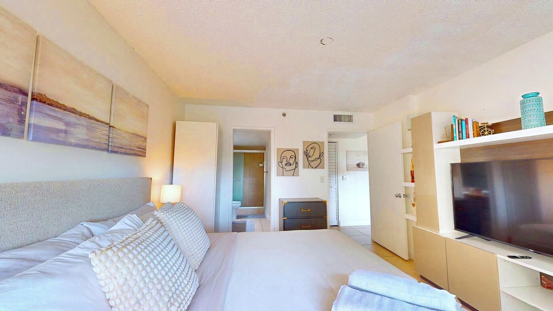 Une chambre d’hôtel avec un grand lit, une télévision, une armoire et une salle de bain visible à travers une porte ouverte.