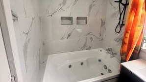 A bathroom with a marble wall, a bathtub, a shower, and a curtain. - The Blackhorse Hotel (Christchurch)