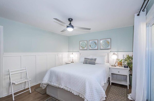 A bedroom with a bed, a nightstand, a ceiling fan, and wall art.