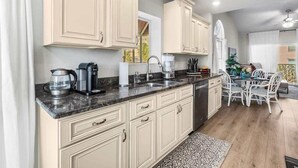Cucina con mobili color beige, un piano di lavoro in marmo e zona pranzo con sedie bianche.