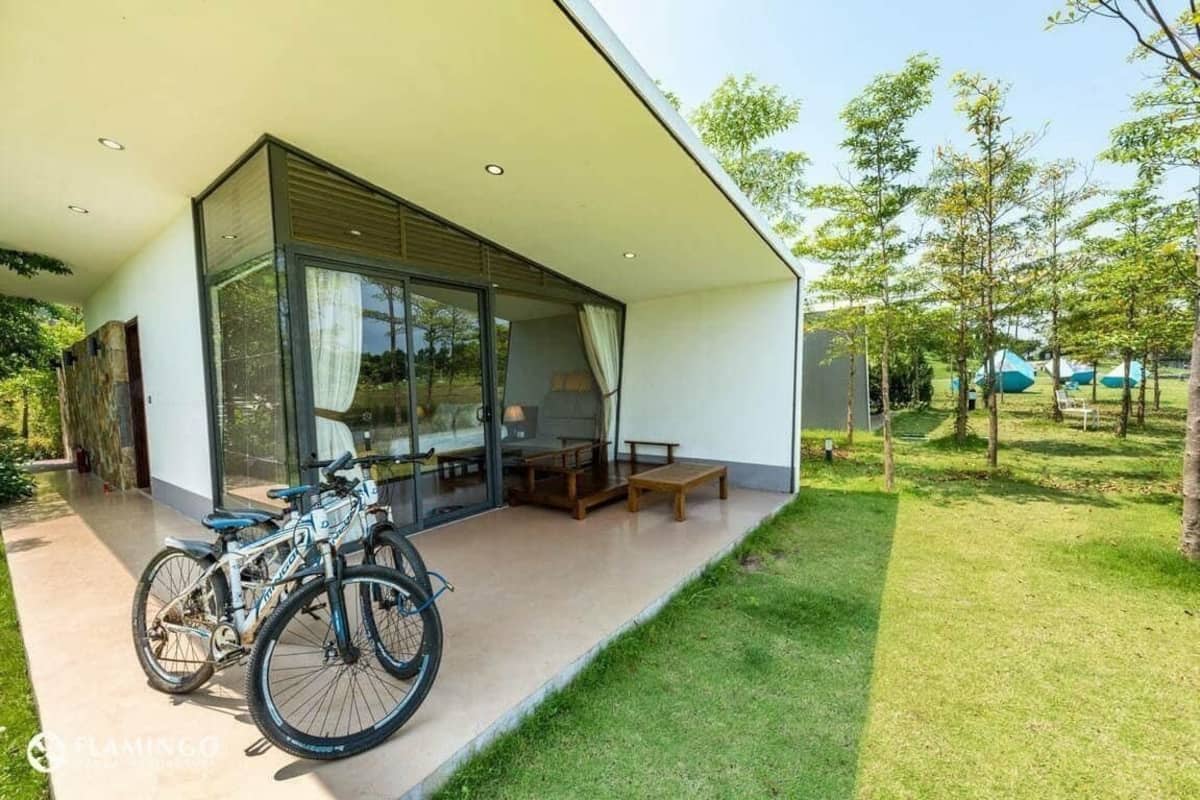 A modern house with a glass door entrance, a patio with a table and chairs, and a bicycle parked outside.