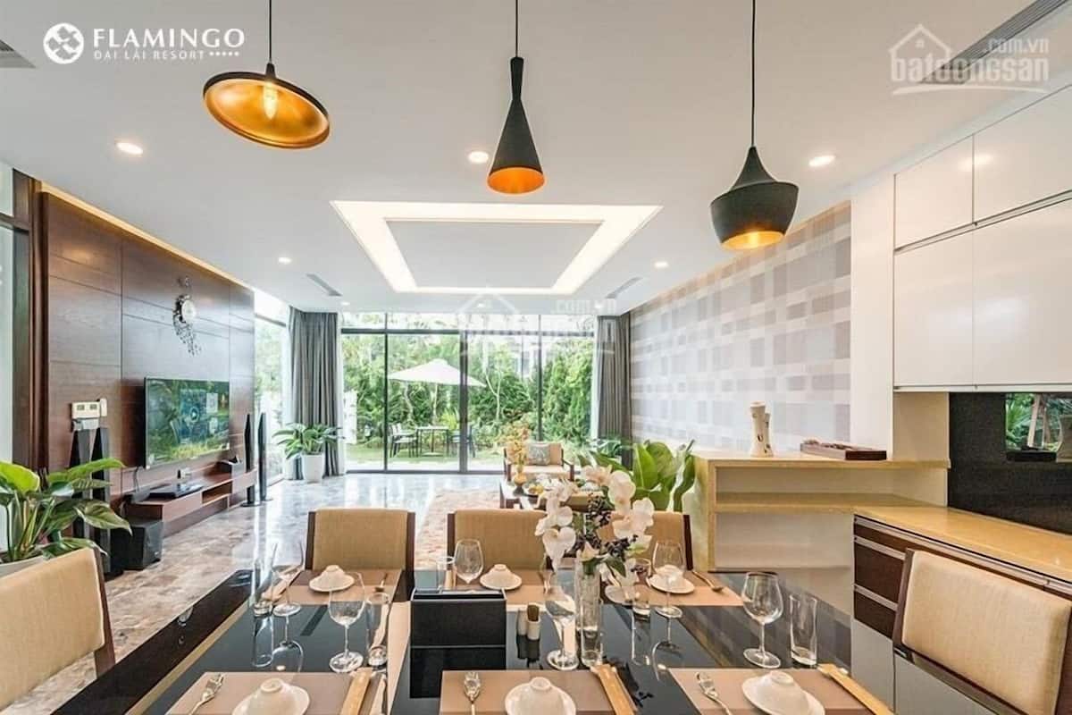 A modern dining area with a long table set for a meal, a TV on the left, and a view of the outdoors.