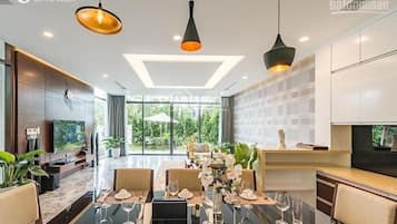 A modern dining area with a long table set for a meal, a TV on the left, and a view of the outdoors.