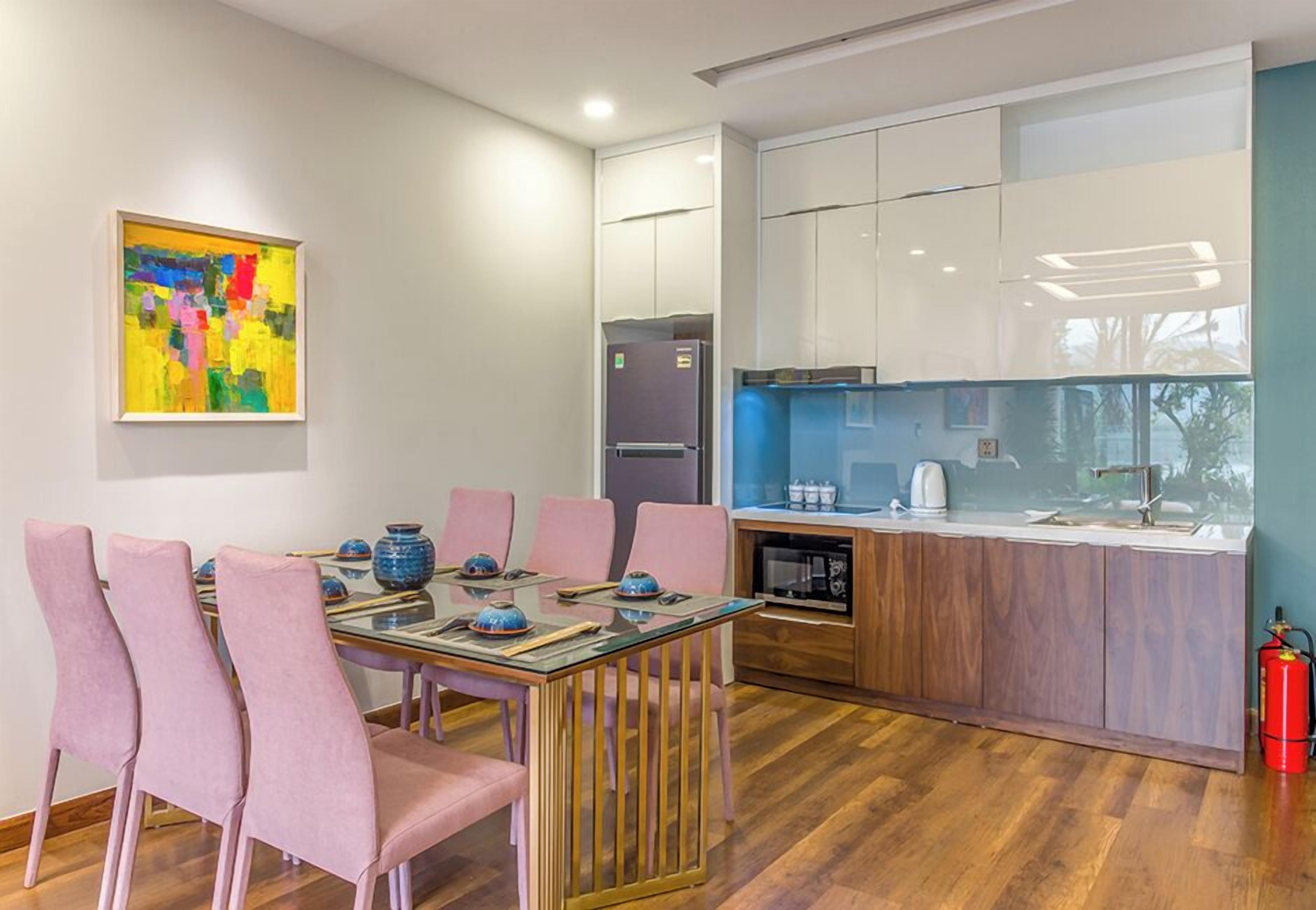 Een moderne keuken met witte kastjes, een inbouwoven en een glazen eettafel met roze stoelen.