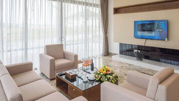 A modern living room with a sofa set, a coffee table with tea cups and a flower arrangement, and a flat-screen TV mounted on the wall.