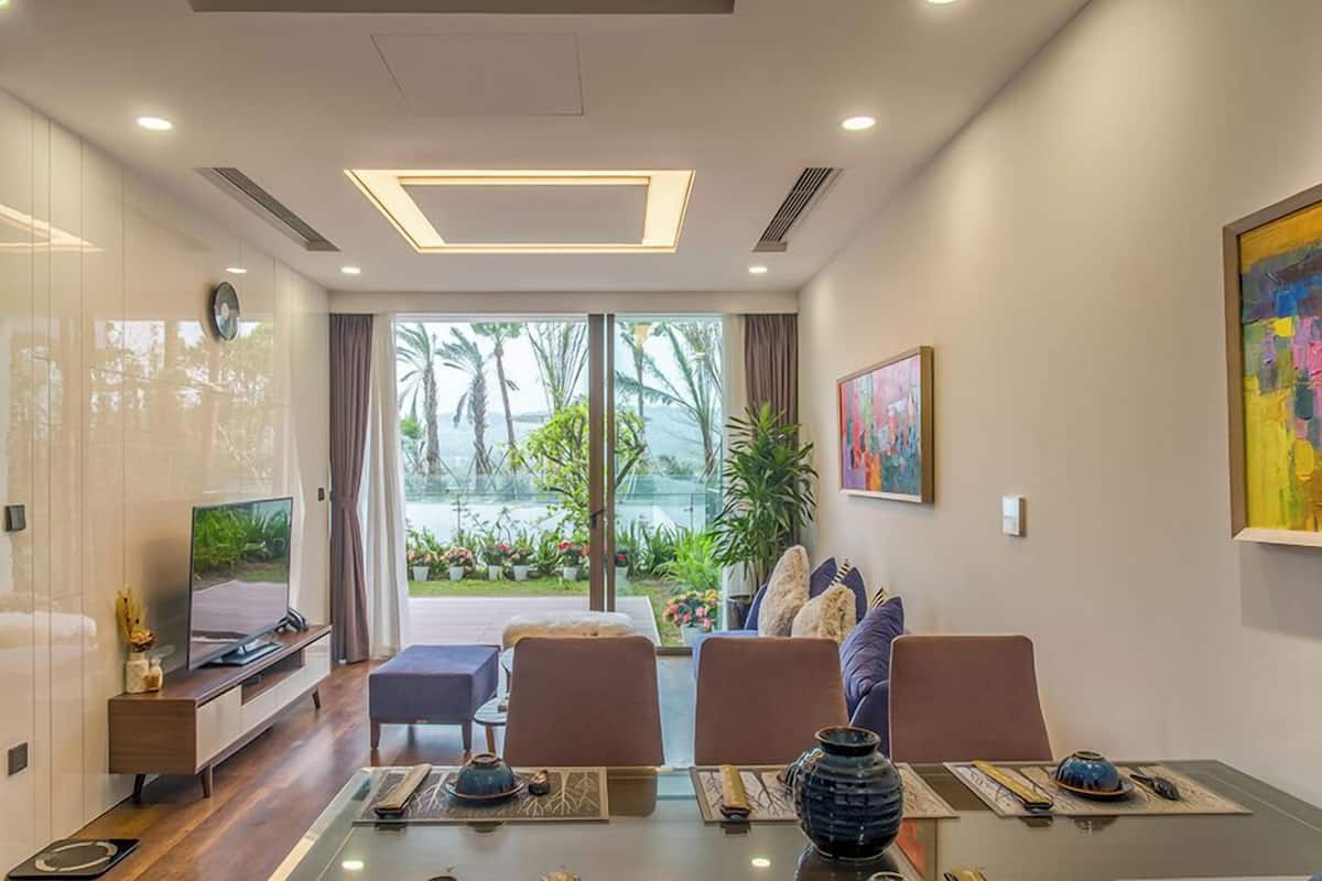 A modern living room with a glass coffee table, comfortable seating, a television, and a view of palm trees through large windows.