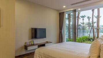 Habitación de hotel con una cama grande, un televisor de pantalla plana sobre un mueble de madera y un balcón con vistas a palmeras.
