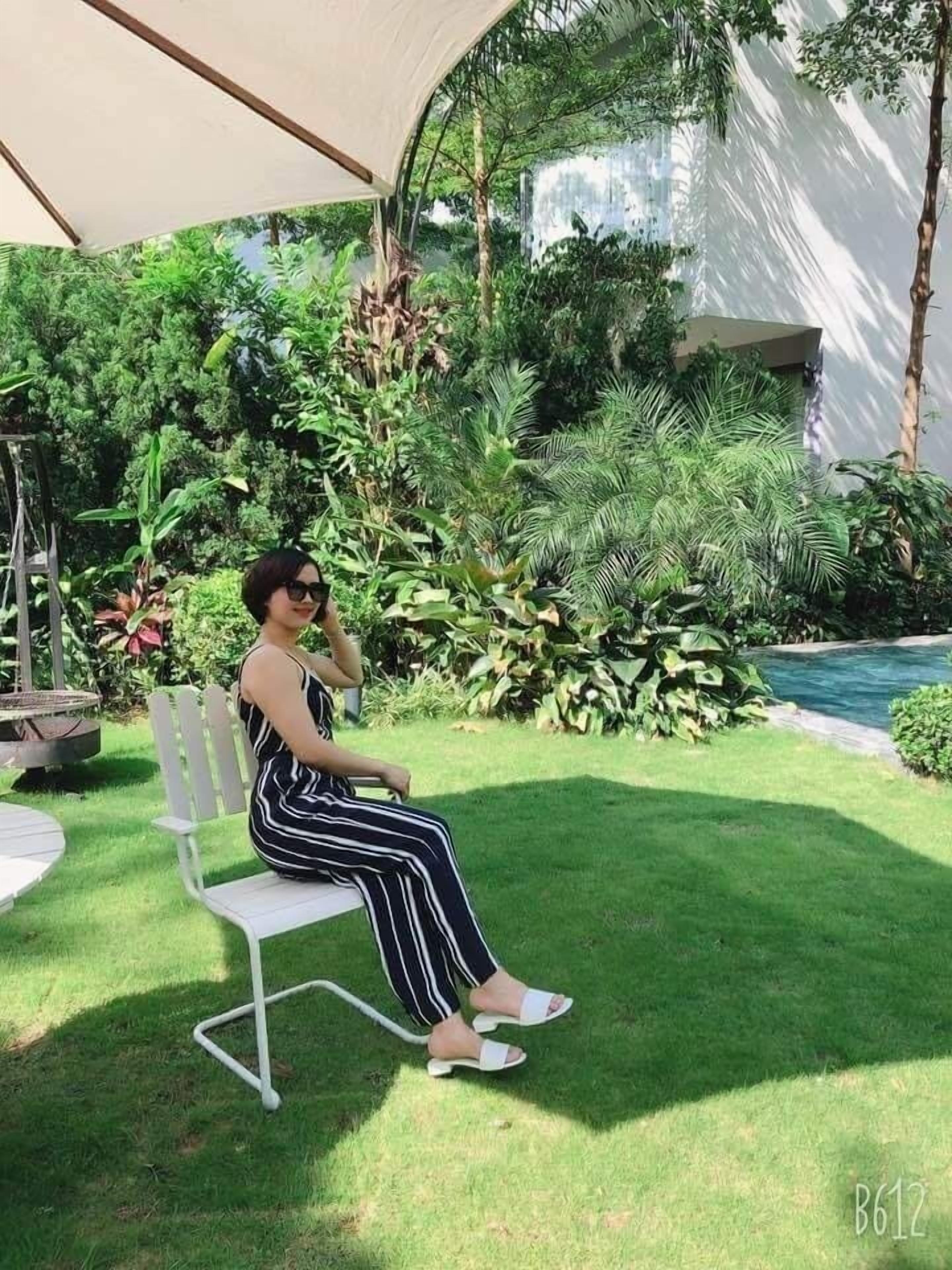 Una persona sentada en un banco blanco en un jardín exuberante con diversas plantas y una fuente al fondo.