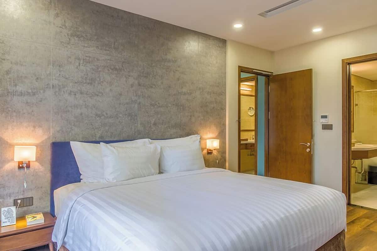 A modern hotel room with a large bed, two bedside lamps, a wooden door, and a bathroom visible through an open door.