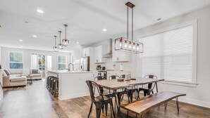 A modern kitchen with white cabinets, a wooden dining table, and black chairs. - Bethany Beach * New Modern Luxurious Townhome - 4 (Ocean View)