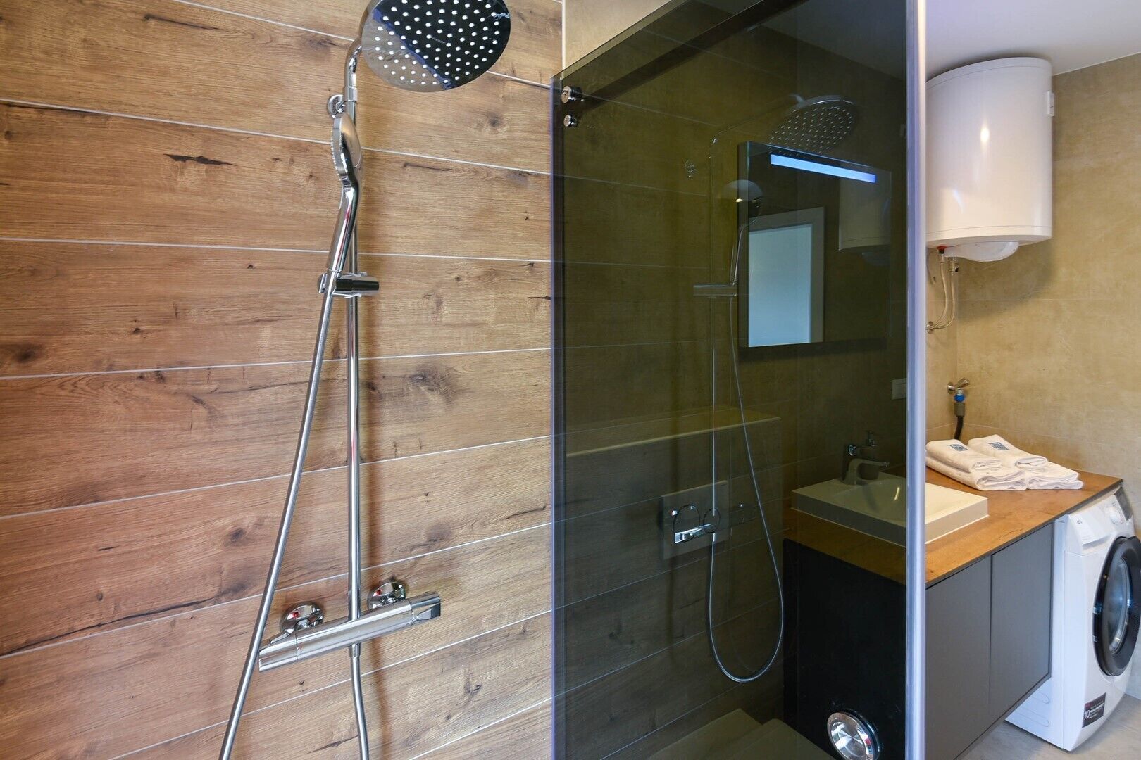 A modern bathroom with a wooden wall, a glass shower enclosure, a sink, and a washing machine.