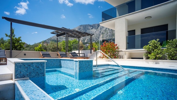 Ein moderner Poolbereich im Freien mit einer Pergola, Liegestühlen und Blick auf die Berge.