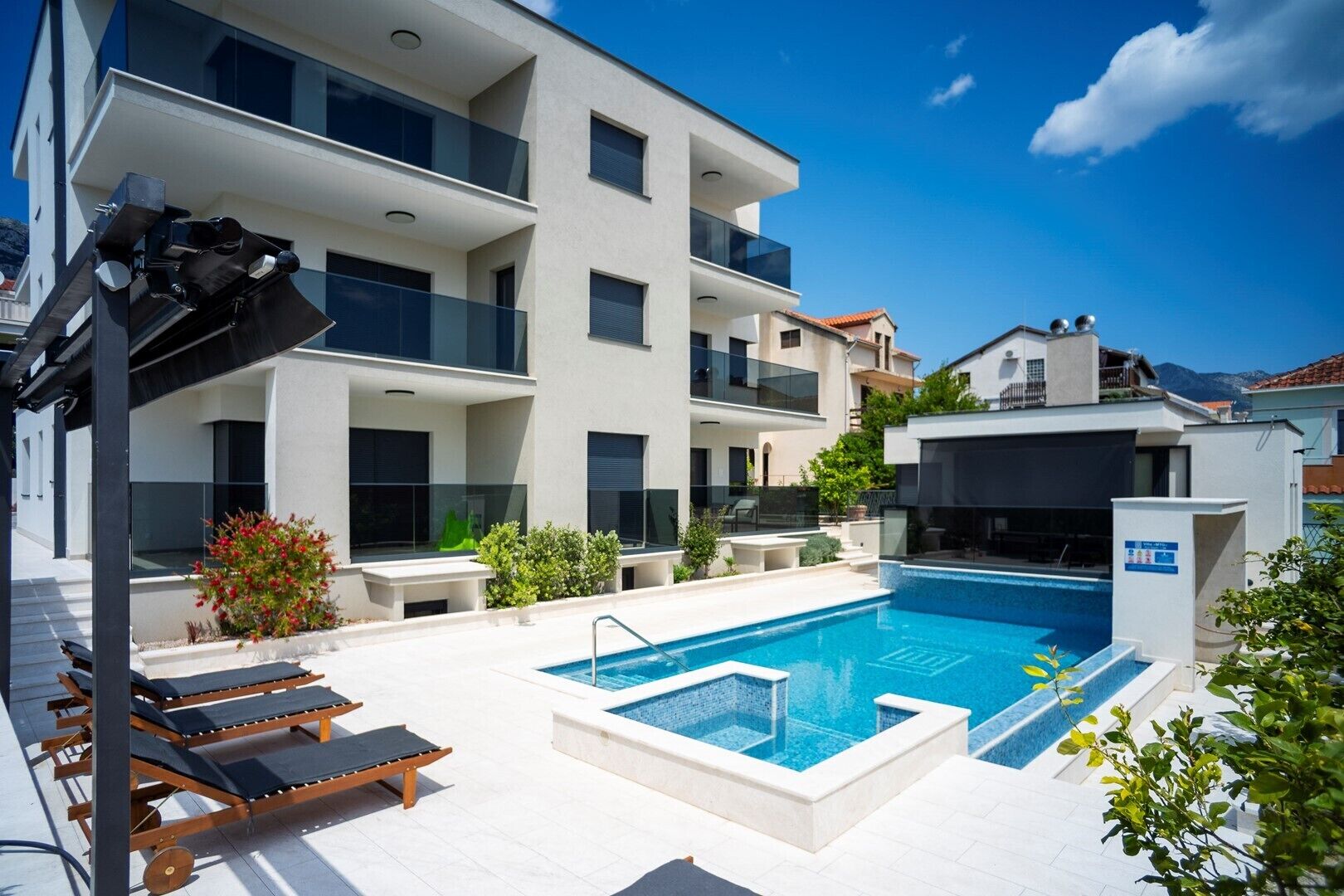 A modern multi-story building with a swimming pool, outdoor seating, and a clear blue sky.