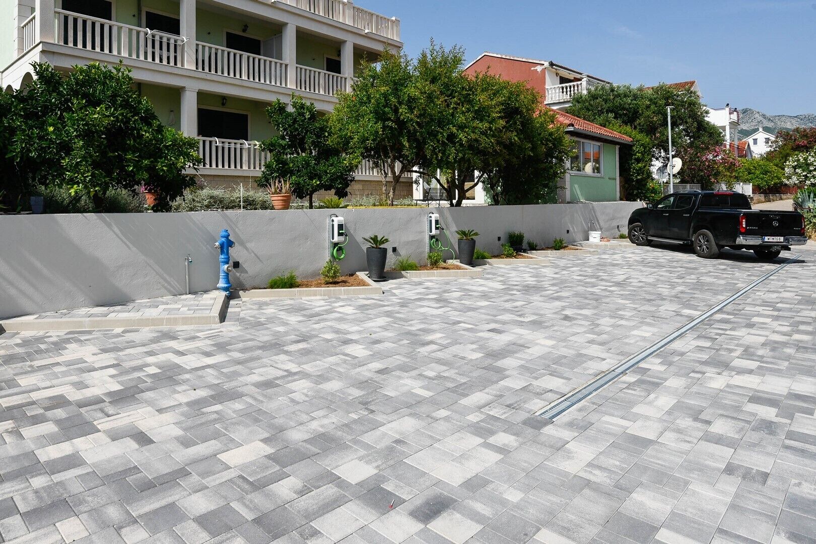 Zona exterior pavimentada amb un hidrant blau, una pickup negra i un edifici amb balcons al fons.