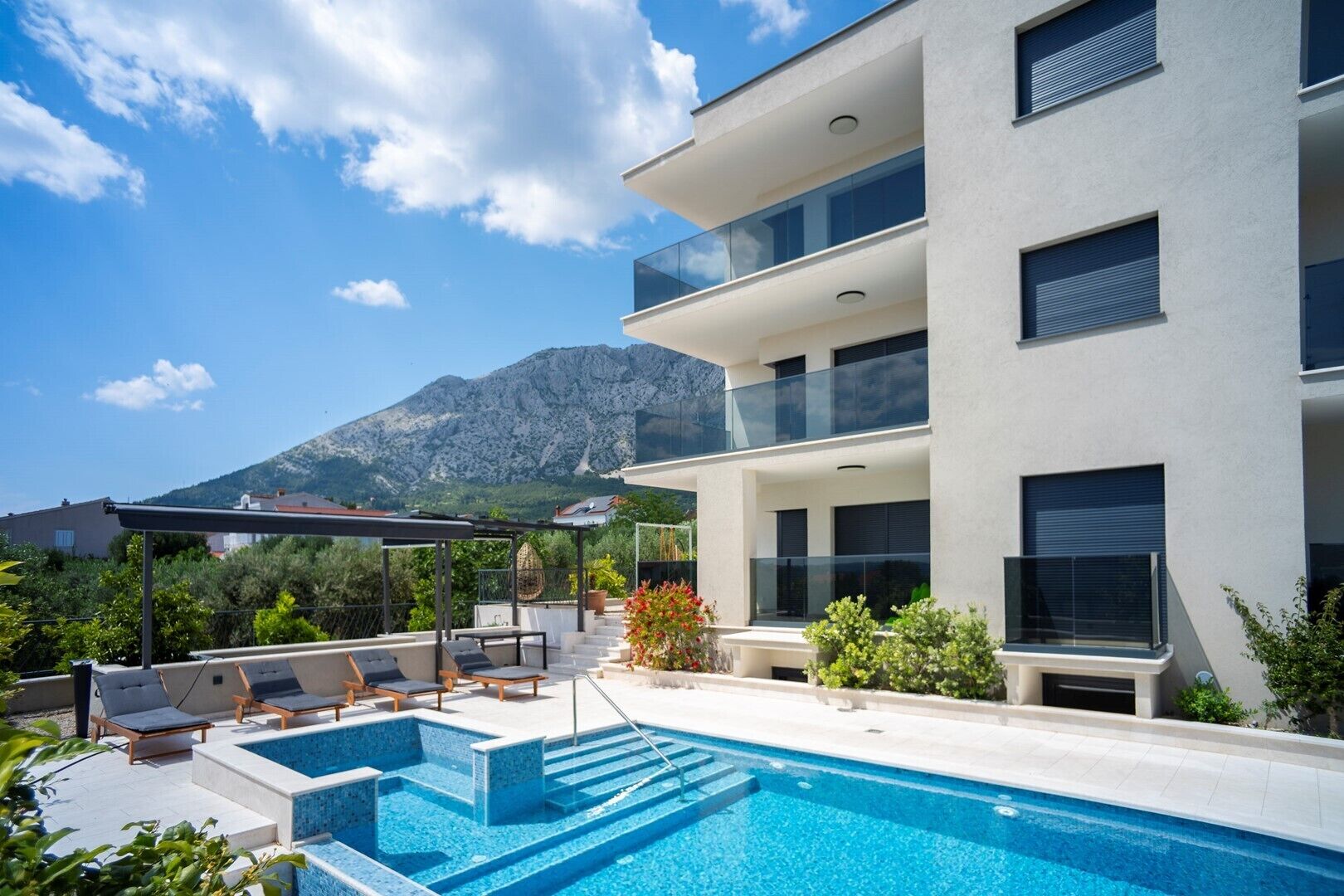 Ein modernes, zweistöckiges Gebäude mit Pool auf dem Dach, Außenbereich mit Sitzgelegenheiten und Blick auf die Berge.