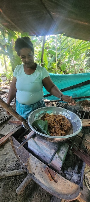 Una persona cocinando al aire libre, con un tazón de metal sobre una estufa improvisada.