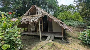A rustic hut with a thatched roof, wooden deck, and a single door.