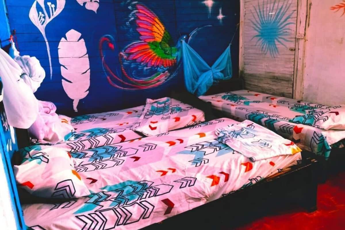 Een kamer met twee bedden, elk voorzien van beddengoed met een patroon en een kleurrijke muurschildering.