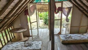 A dormitory room with four beds arranged in a row, a wooden floor, and a thatched roof.