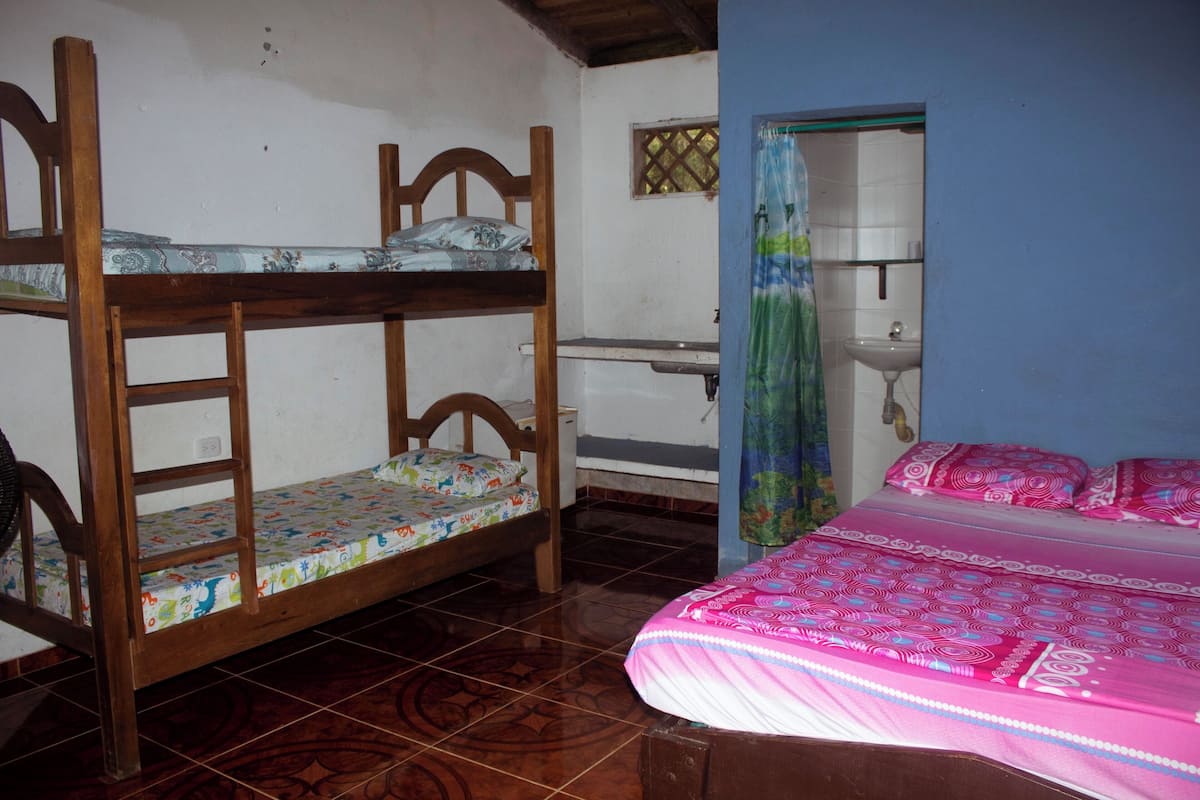 Een kamer met een stapelbed, een enkel bed, een klein tafeltje met een wastafel en een raam met gordijn.