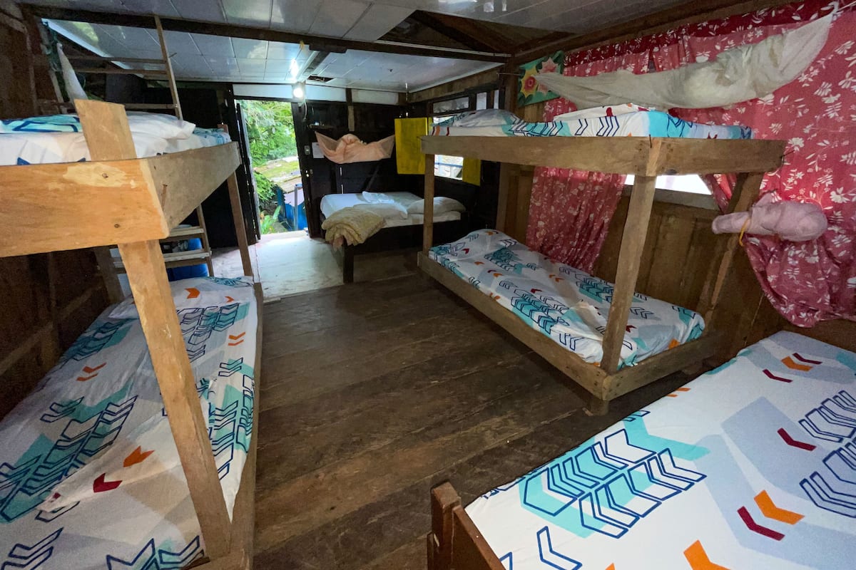 Een studentenkamer met stapelbedden, een houten vloer en een raam met gordijnen.