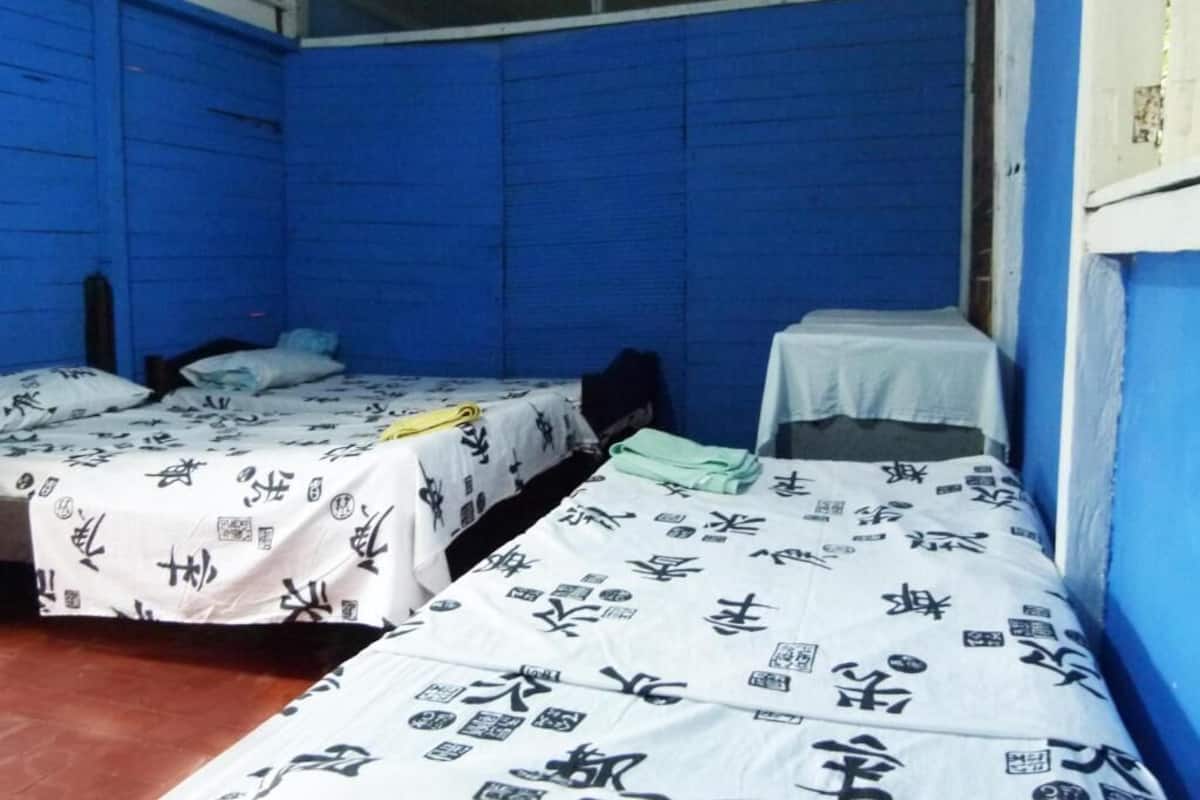 Een kamer met twee bedden, elk met een wit laken met zwarte kalligrafie. De muren zijn blauw en er is een raam aan de rechterkant.