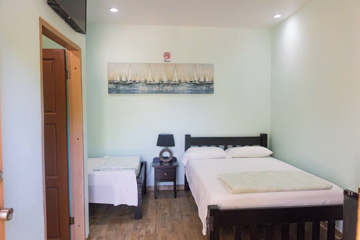 A bedroom with a bed, a nightstand, a lamp, and a painting of sailboats on the wall.
