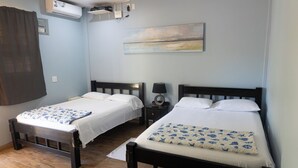 Une chambre avec deux lits, un climatiseur fixé au mur, une petite table de chevet avec une lampe et un tableau au-dessus des lits.