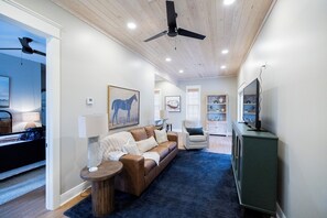 A modern living room with a brown leather sofa, a round coffee table, and a blue rug. There is a ceiling fan, recessed lighting, and a green cabinet. - Historic District Gem | Walk to Downtown Laurel (Laurel)