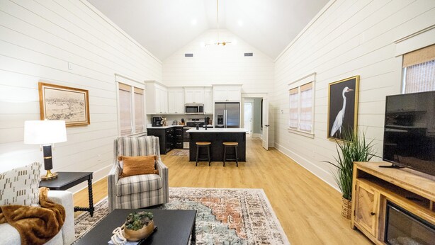 Un salón amplio con chimenea, comedor y cocina con muebles blancos y electrodomésticos modernos.