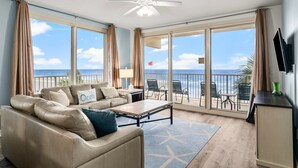 A spacious living room with a sofa, coffee table, and a balcony with a view of the ocean. - Beachfront resort condo - pool, hot tub & gym (Panama City Beach)