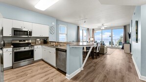 A modern kitchen with stainless steel appliances, a dining area with a view, and a balcony with a view. - Beachfront resort condo - pool, hot tub & gym (Panama City Beach)