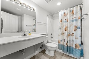 A bathroom with a white sink, mirror, and toilet. It has a shower curtain with a nautical theme. - Beachfront resort condo - pool, hot tub & gym (Panama City Beach)