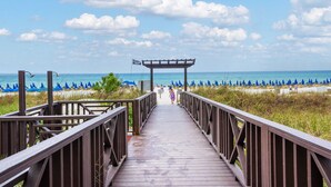 A wooden boardwalk leading to a beach with blue umbrellas and a clear sky. - Shores of Panama - pools, hot tub and daily perks (Panama City Beach)