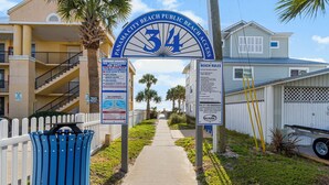 A pathway leading to a beach entrance with a sign indicating beach access number 34, palm trees, and a white picket fence.