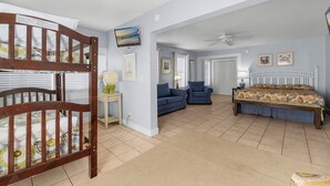 A spacious room with a bunk bed, a sofa, a bed with a floral bedspread, a television, and a ceiling fan.