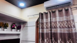 A bathroom with a shower curtain, an air conditioning unit, and a shelf with potted plants. - Vatsalya Bhawan Ayodhya (Faizabad)