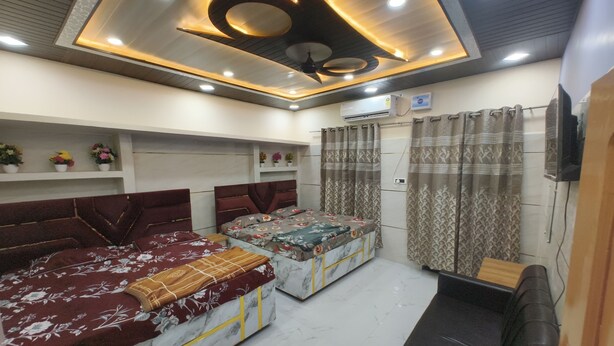 A modern bedroom with two beds, a ceiling fan, and a TV mounted on the wall. - Vatsalya Bhawan Ayodhya (Faizabad)