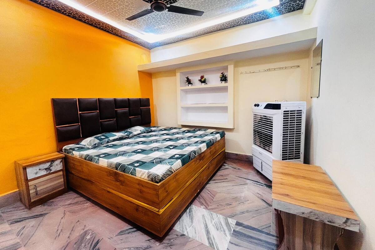 Un dormitorio con cama de madera, ventilador de techo, estante montado en la pared con objetos decorativos y unidad de aire acondicionado.