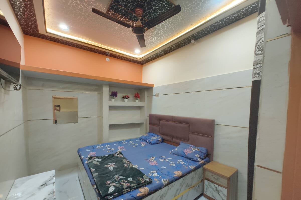 Un dormitorio con cama, mesita de noche, ventilador de techo y estante con flores.