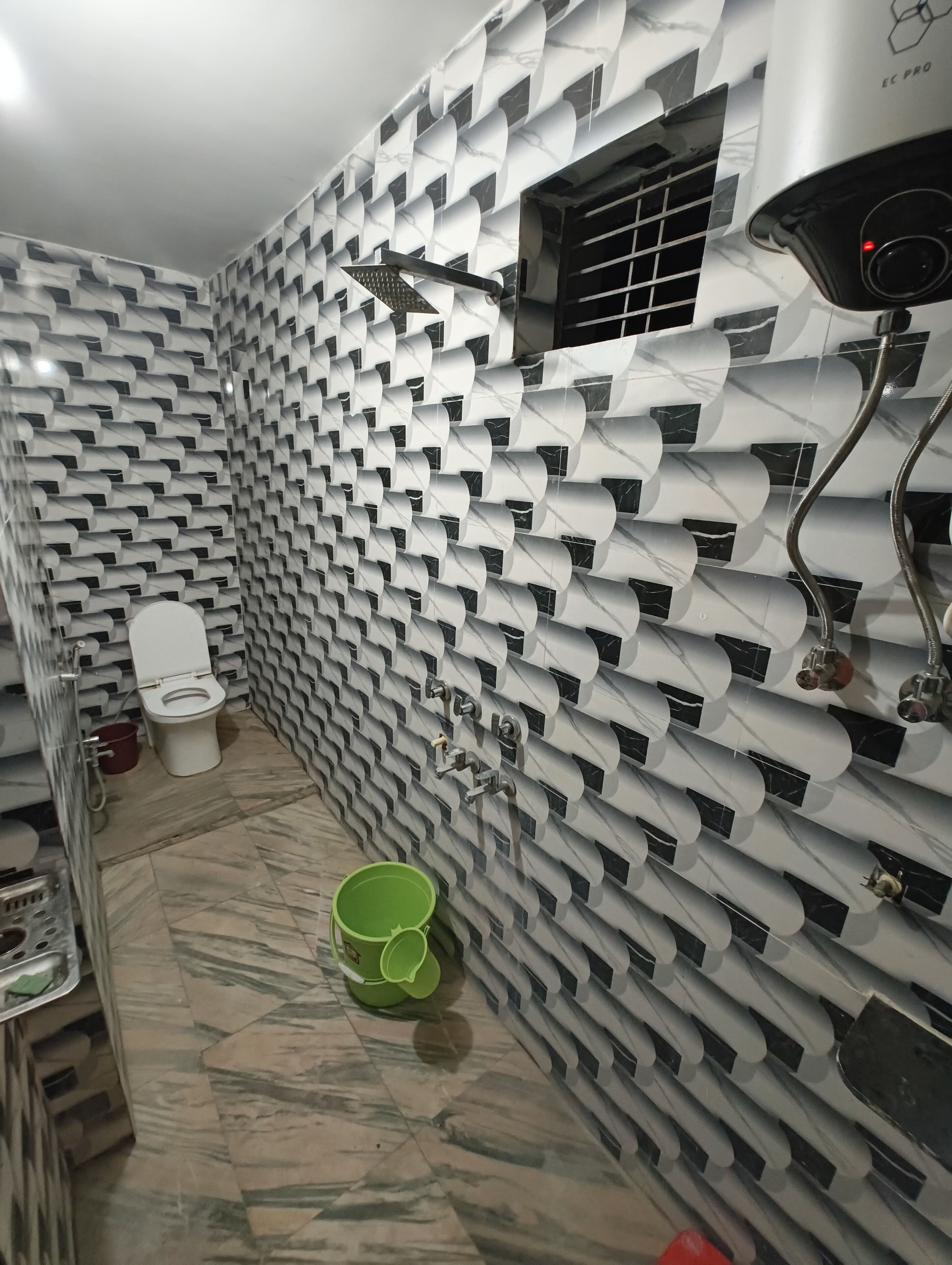 A bathroom with a unique wall design, a toilet, a green bucket, and a shower area.