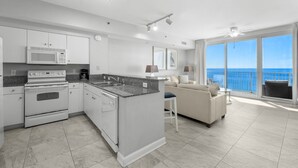 Cocina moderna con electrodomésticos blancos, comedor con mesa y sillas blancas, y un balcón con vistas al océano.