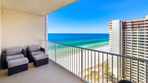 A balcony with wicker furniture overlooking a beach and a hotel building. - Modern condo w/ resort amenities & Gulf views (Panama City Beach)