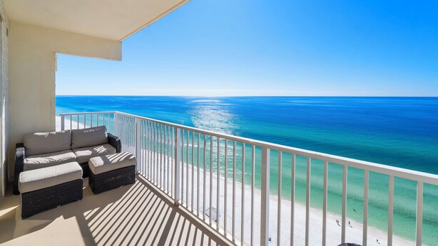 A balcony with a view of the ocean, a white railing, and a sofa with cushions.