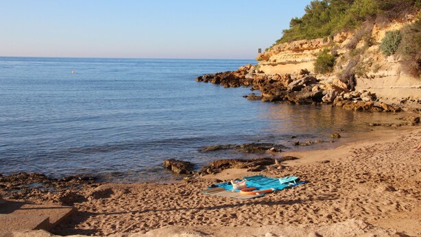 Une plage bordée d’un rivage rocheux, un ciel dégagé et une mer calme.