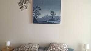 Une chambre à coucher comprenant un lit, deux tables de chevet, un luminaire suspendu et un tableau représentant un paysage accroché au mur.