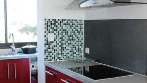 Une cuisine avec des meubles de couleur rouge, une cuisinière noire et un dosseret carrelé.